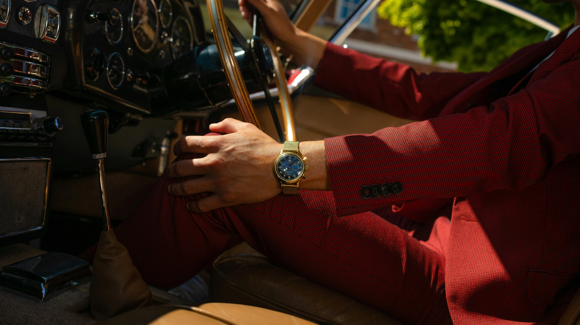 Man in red suit wearing luxury watch driving classic car